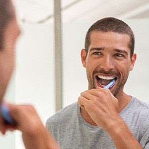 A happy, smiling man brushing his teeth in front of a mirror