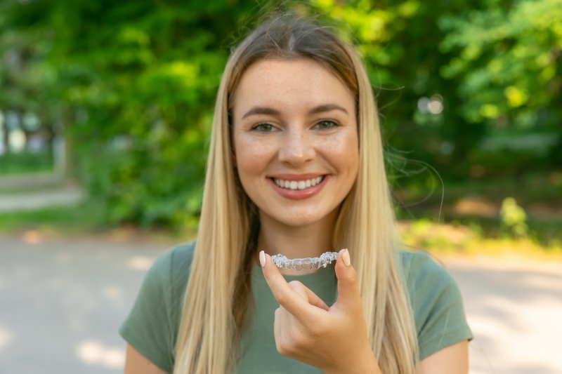A smiling woman holding a clear aligner outdoors