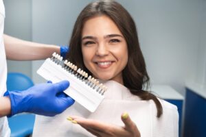 Patient smiling with veneers held up to her mouth in dentist's chair.
