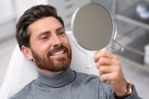 Man smiling into mirror after his smile makeover
